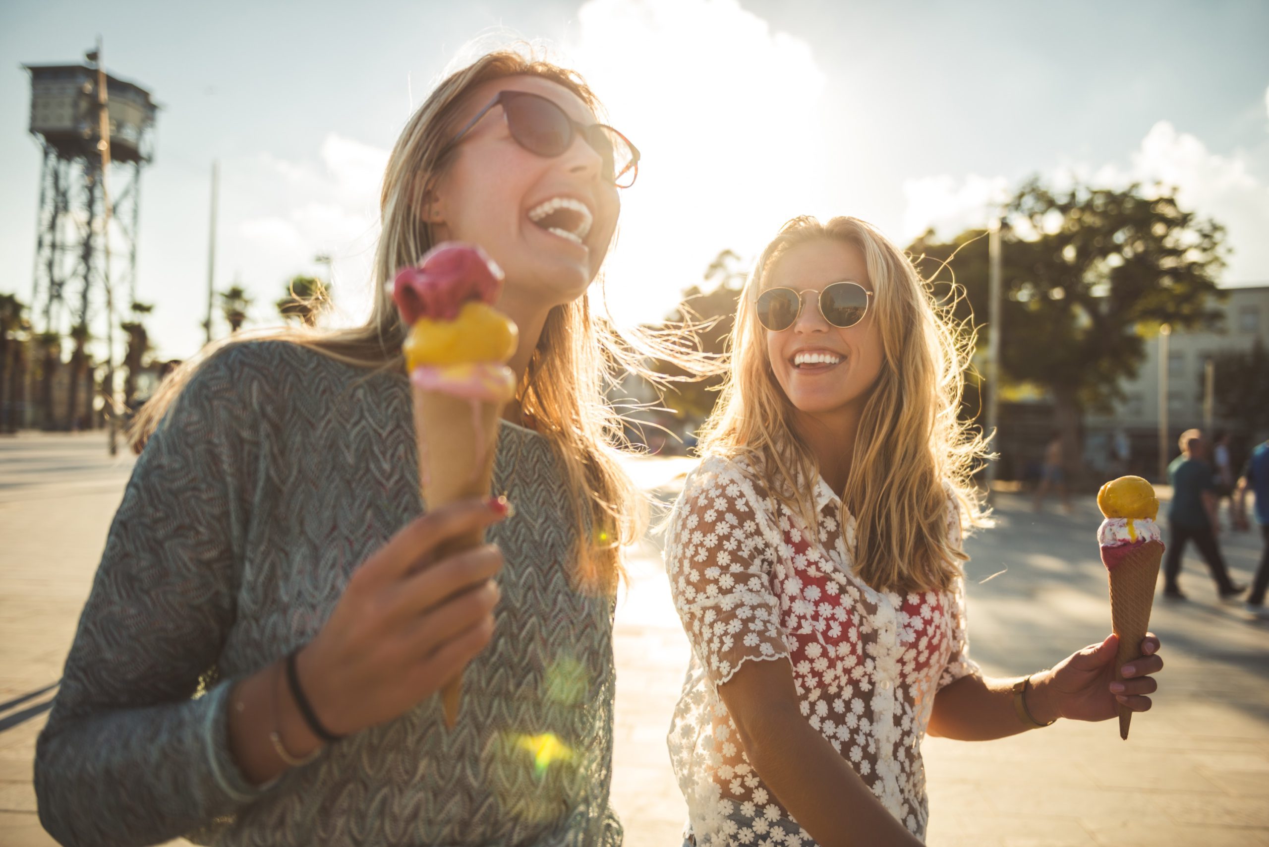 Zwei junge Frauen lachen und essen Eis in der Sonne an einem Sommertag.