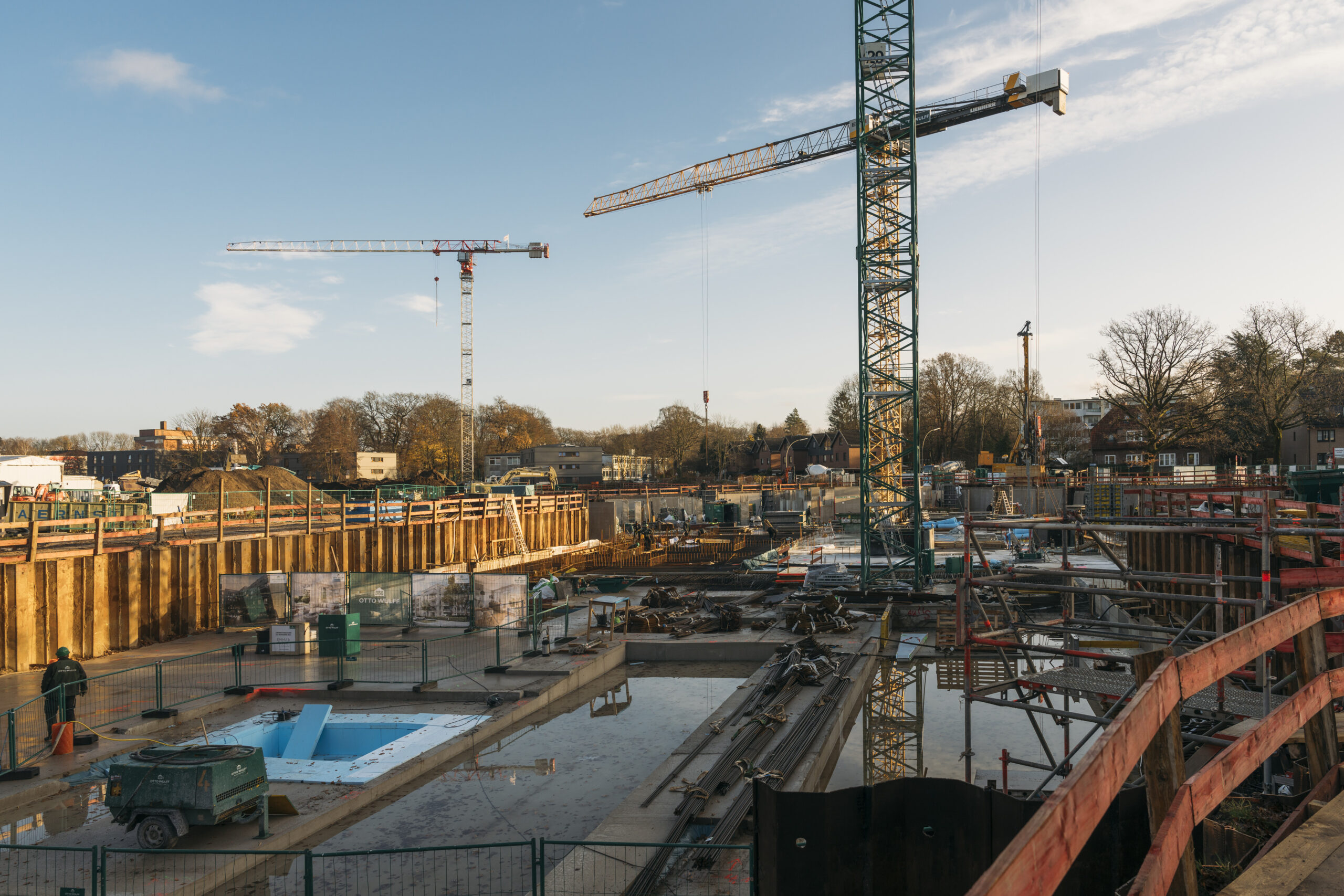 Baustelle mit zwei großen Kränen und Baumaterialien bei Sonnenlicht.