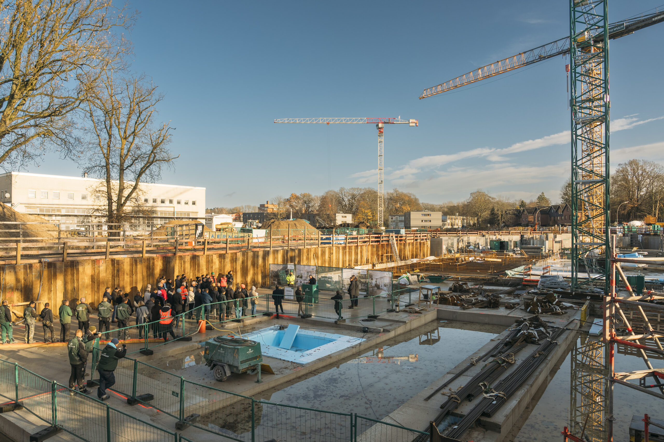 Gruppe von Menschen auf Baustelle mit Kranen und Bauarbeiten bei Sonnenschein.