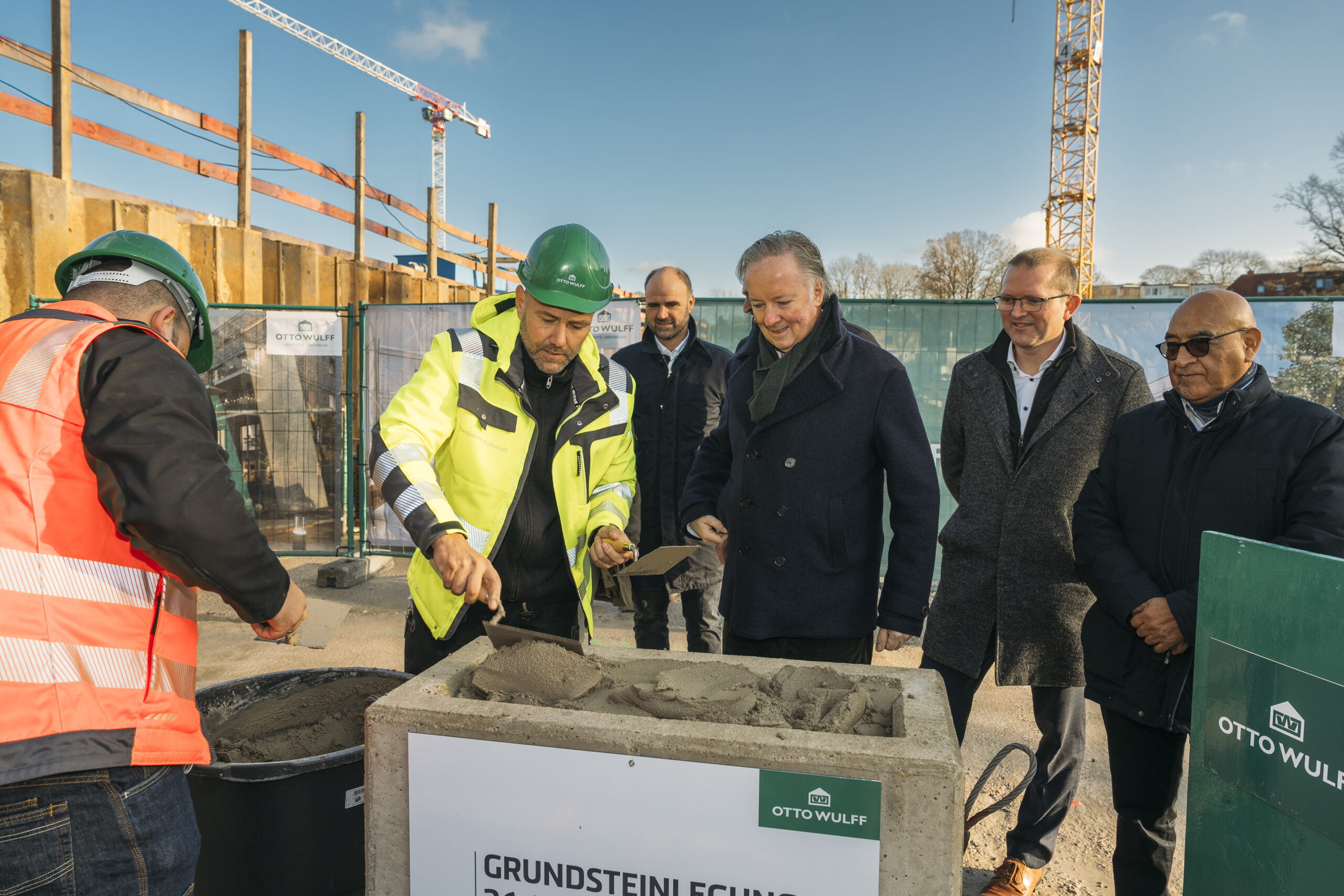 Fünf Männer legen feierlich den Grundstein auf einer Baustelle.