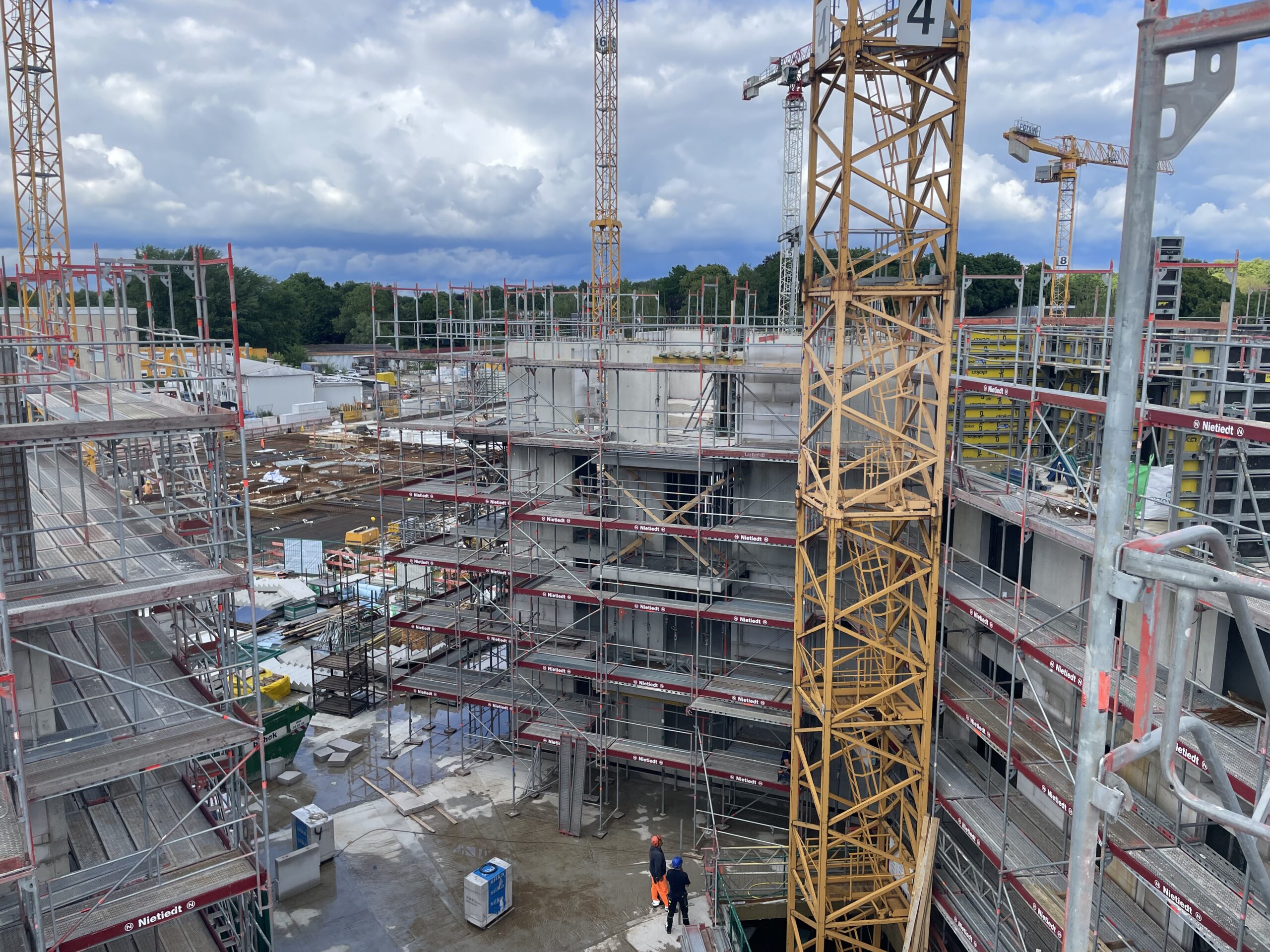 Große Baustelle mit Gerüsten, Kränen und zwei Bauarbeitern im Vordergrund.
