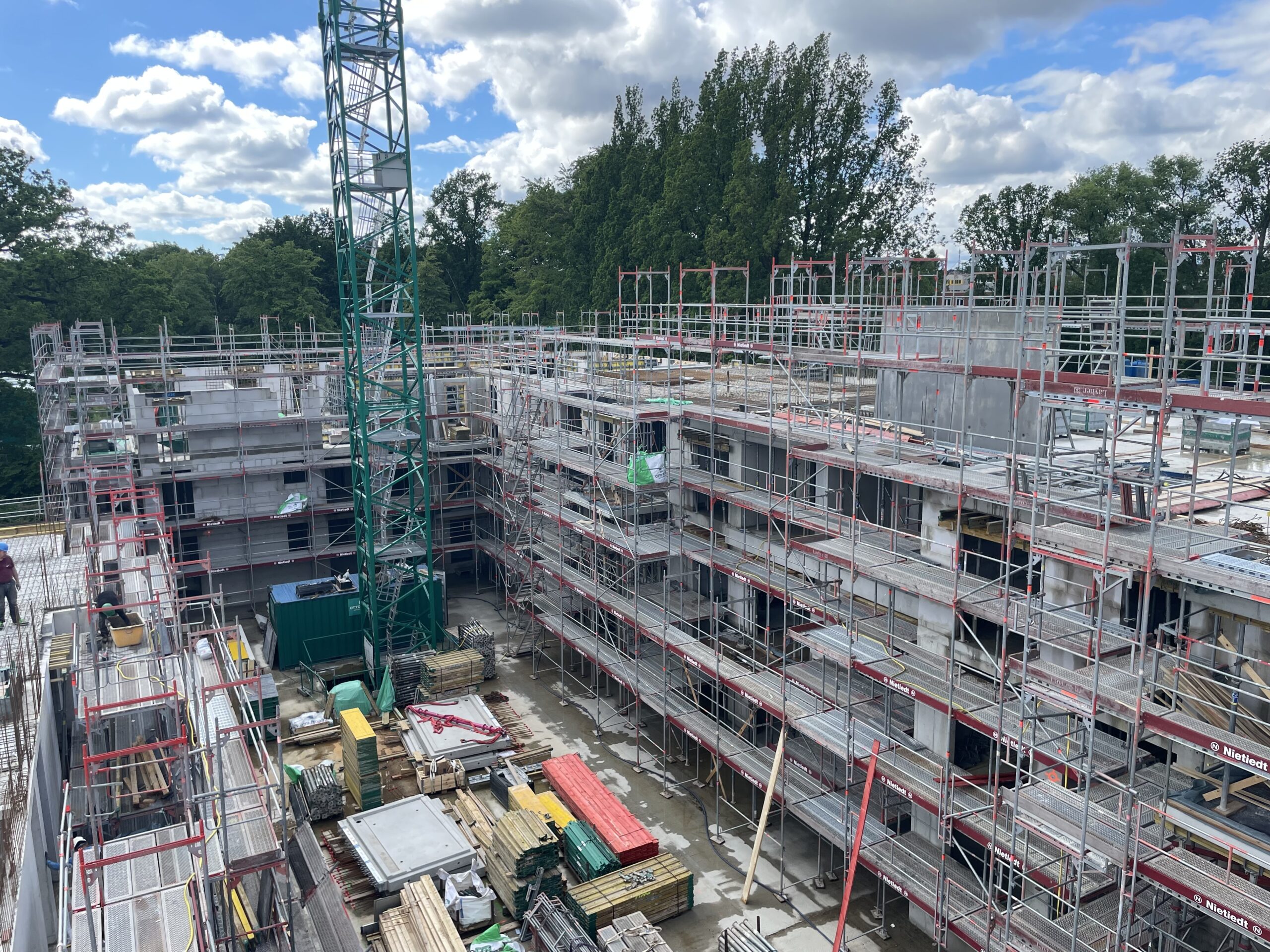 Baustelle eines mehrstöckigen Gebäudes mit Gerüst und Baukran unter Wolken.
