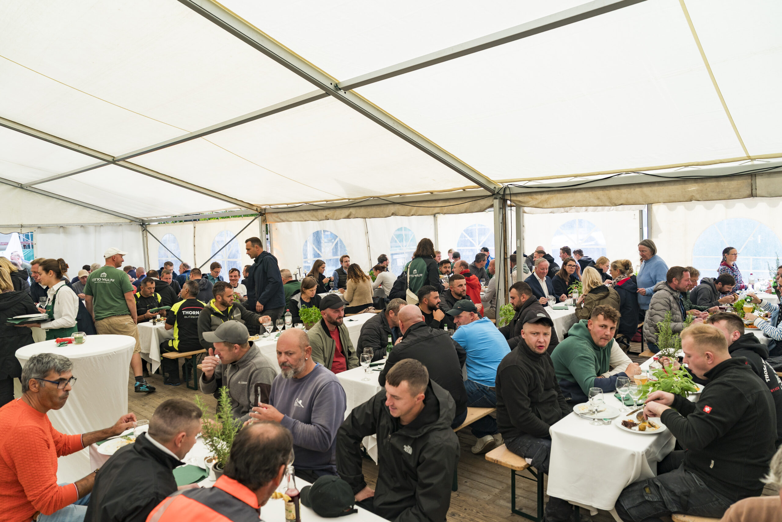 Viele Menschen sitzen in einem Festzelt an Tischen und essen gemeinsam.