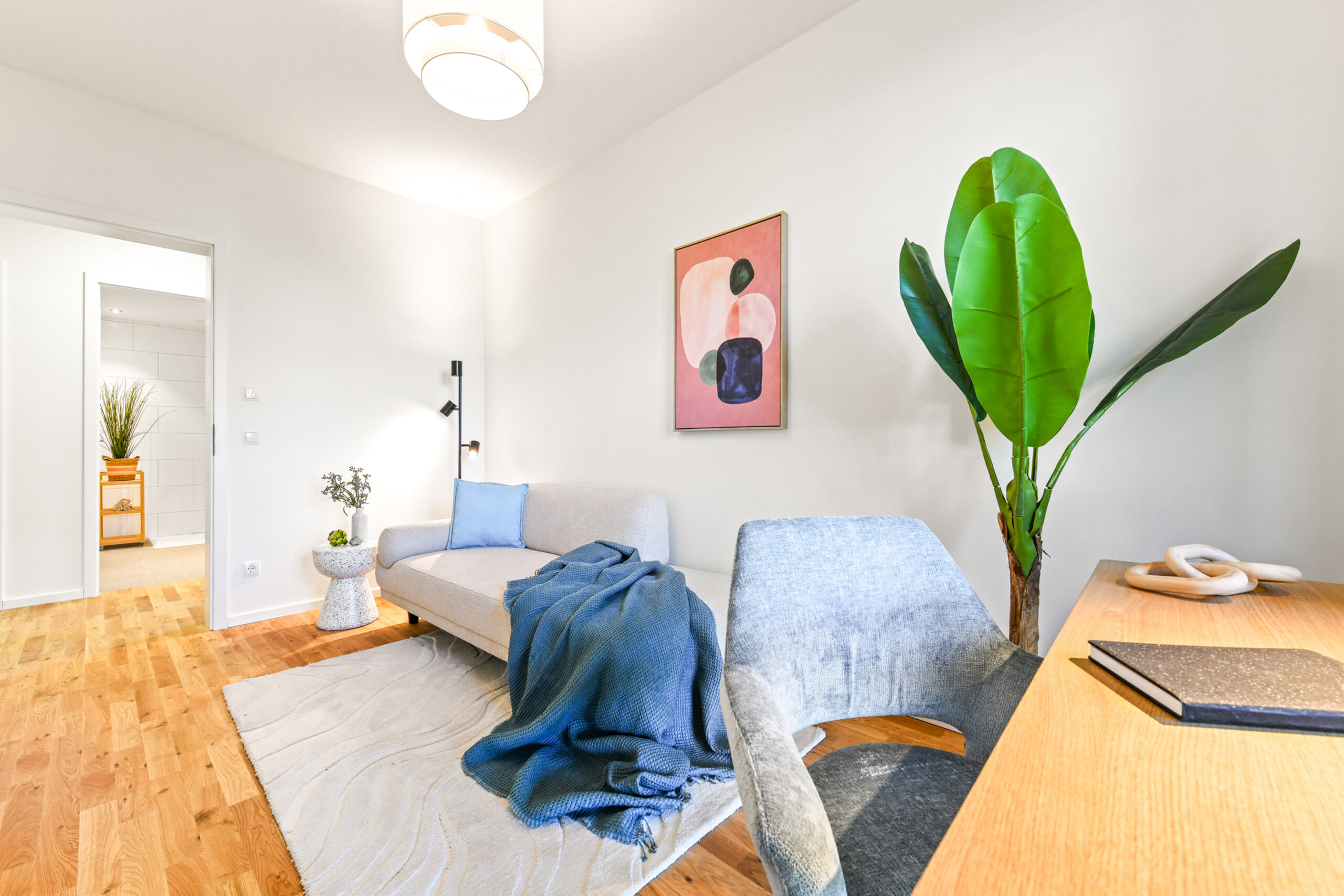 Helles Wohnzimmer mit Sofa, blauem Plaid, Pflanze und Schreibtisch.