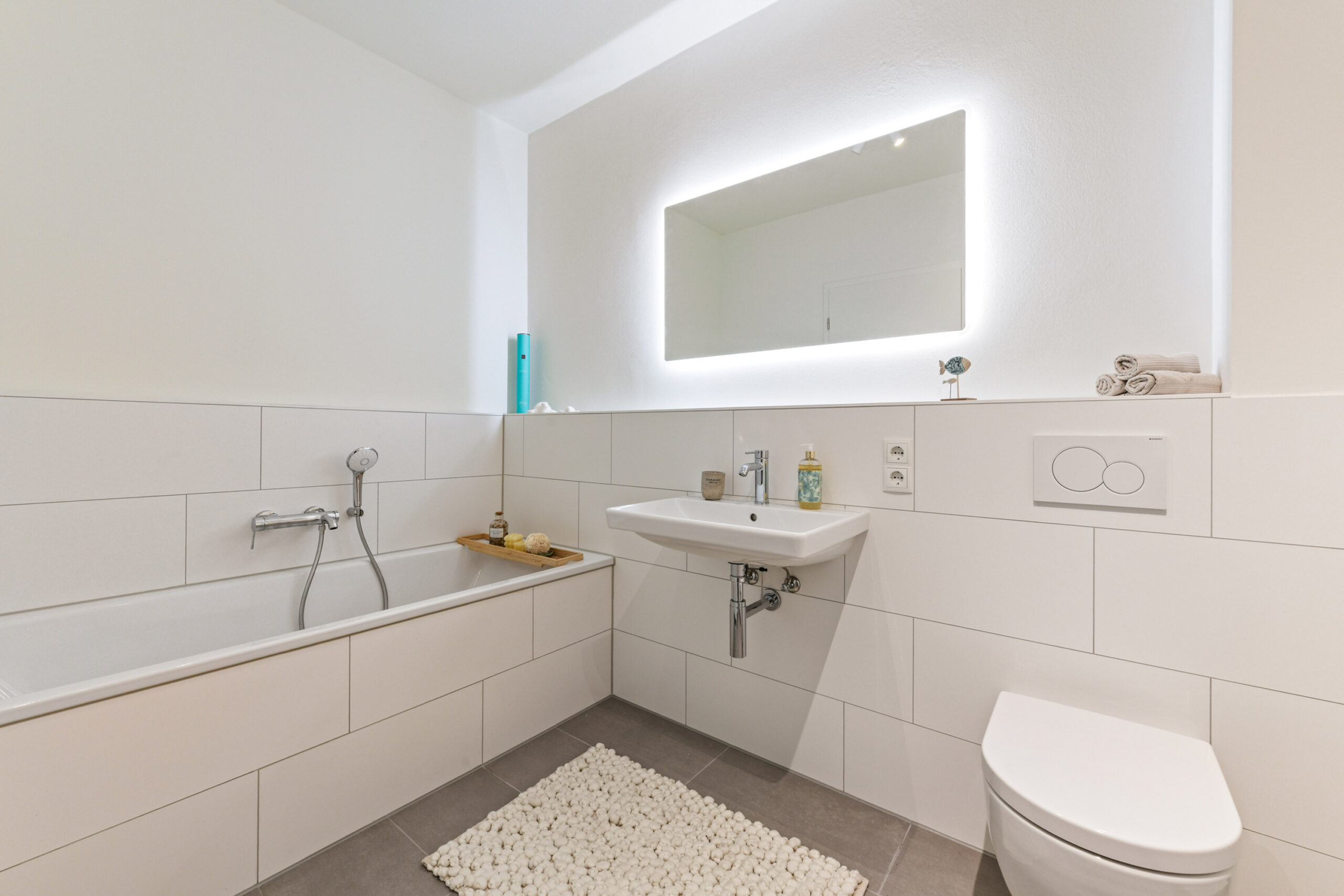 Modernes, weiß gefliestes Badezimmer mit Badewanne, Waschbecken und WC.
