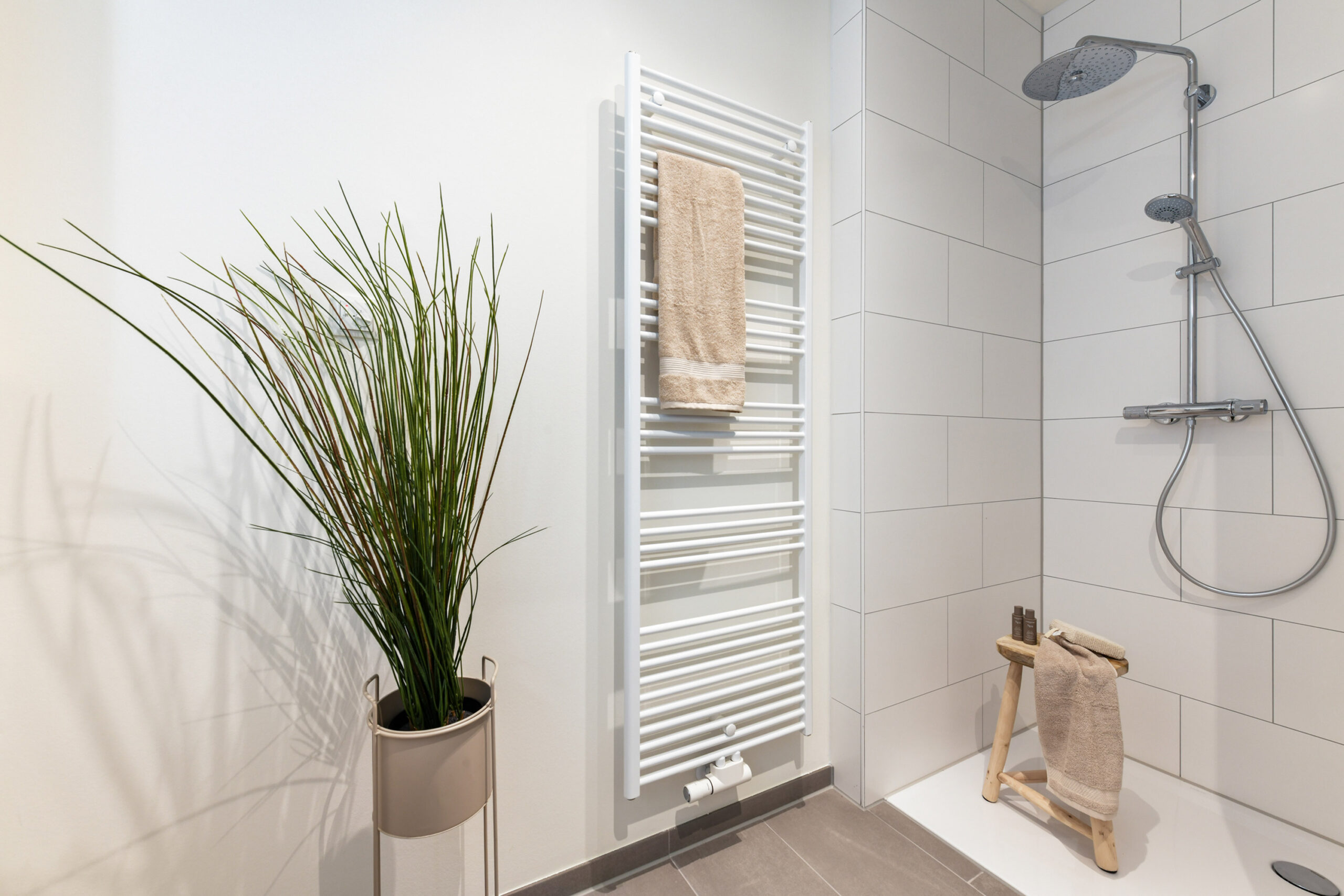 Modernes Bad mit Dusche, Handtuchheizkörper, Hocker, Pflanze und Handtüchern.
