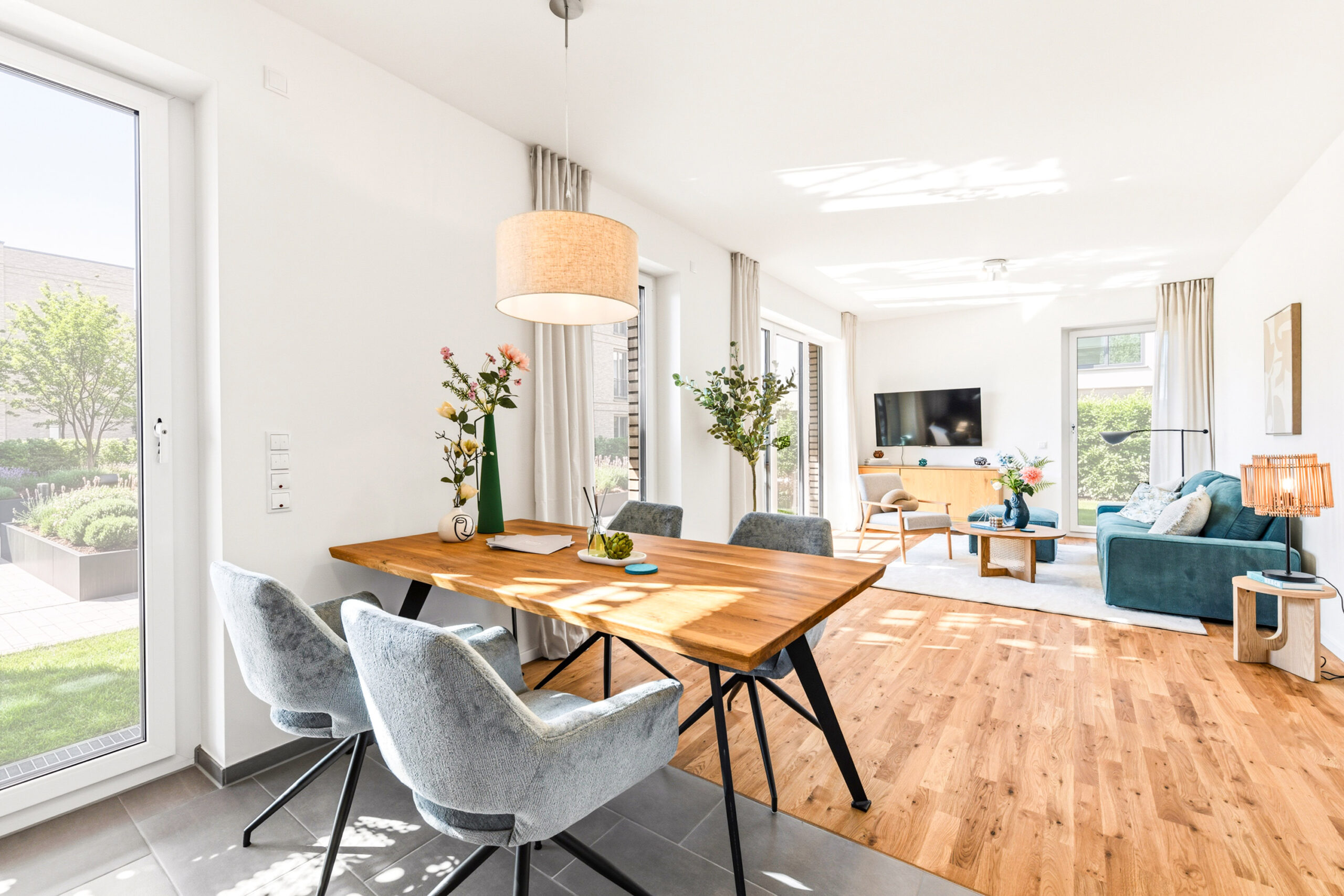 Helles Wohnzimmer mit Holzboden, Esstisch, blauen Sesseln und Sofa.