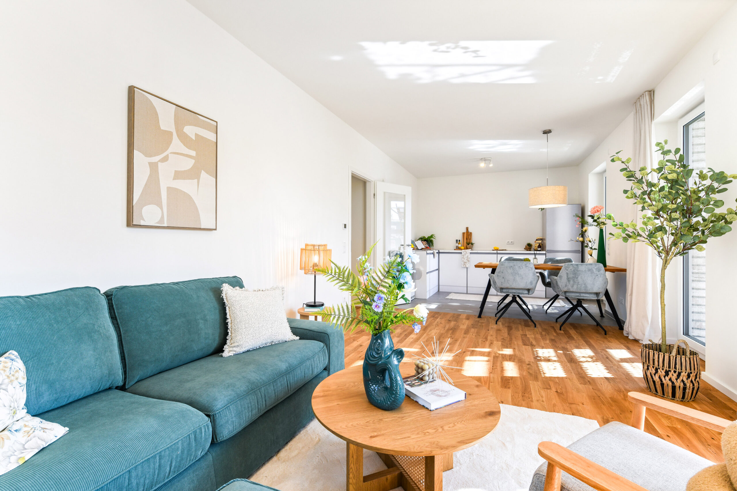 Helles Wohnzimmer mit grüner Couch, Holztisch und offener Küche im Hintergrund.